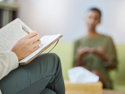 Therapy, therapist notebook and woman listening, help and support of mental health problem and writing notes. Psychology, counseling and psychologist review, analysis and consulting patient or person.